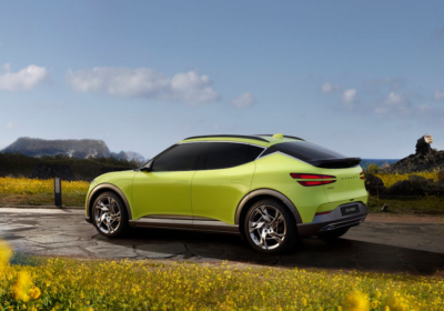 Bright green electric SUV parked on a scenic coastal road with wildflowers in the foreground and mountains in the distance.