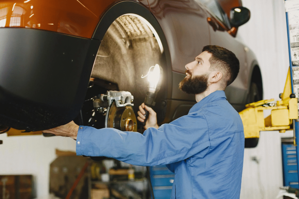 A man is repairing a car in a well-lit garage, surrounded by tools and automotive parts.