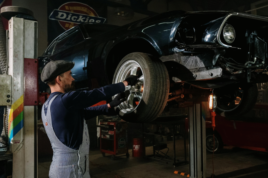 A man is repairing a car in a well-lit garage, surrounded by tools and automotive parts.
