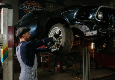 A man is repairing a car in a well-lit garage, surrounded by tools and automotive parts.