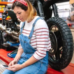 mechanic-woman-looking-phone-sitting-platform-with-motorcycle-factory